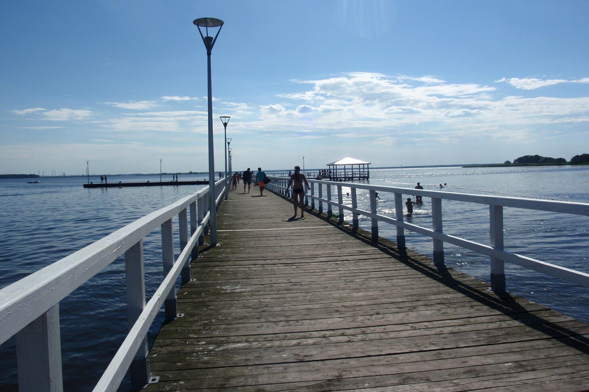 A wooden pier extending into calm water with a white railing, a gazebo, and a clear sky.