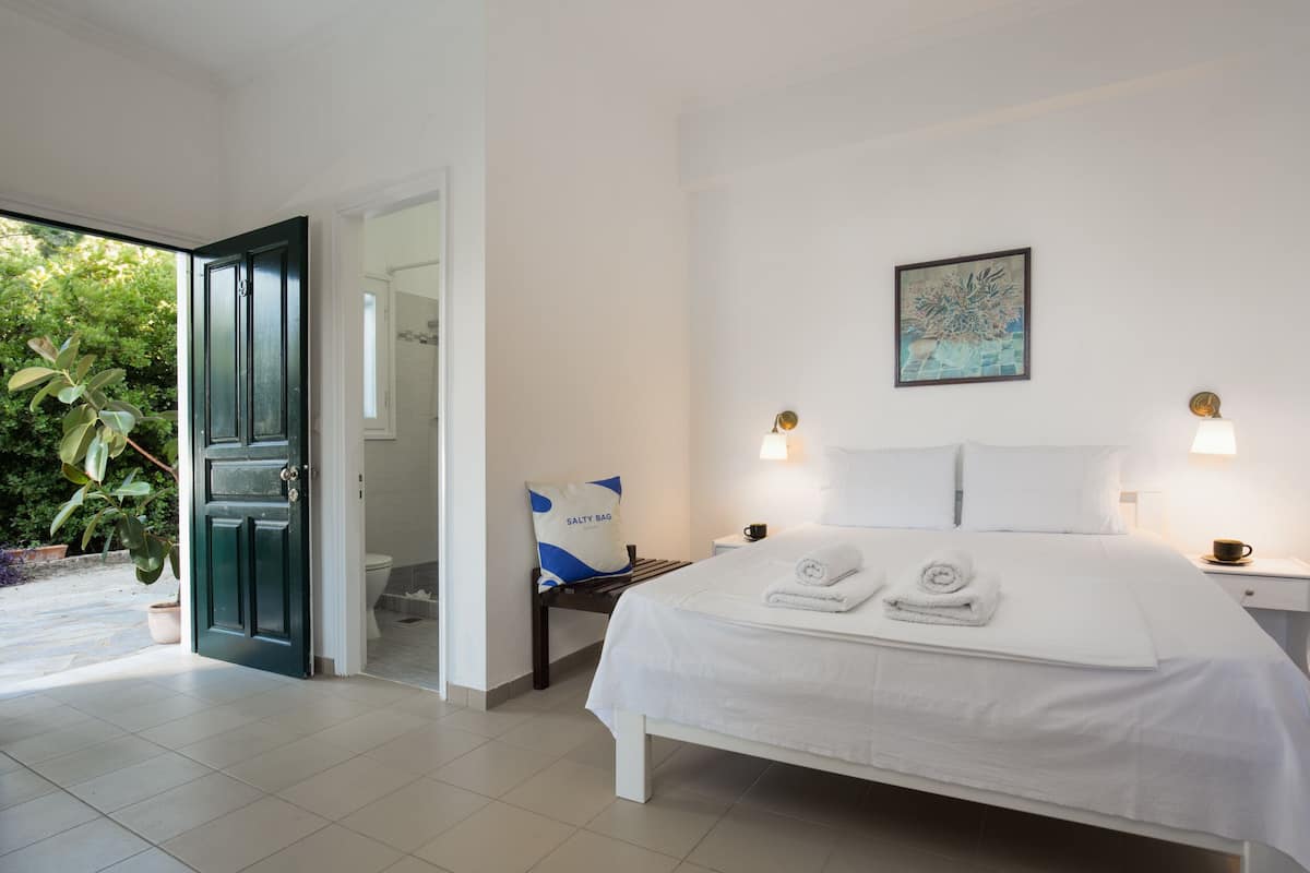 A hotel room with a bed, a nightstand, a bedside table, a pillow, a wall-mounted picture, and a door leading to a balcony.