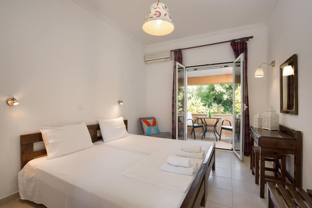 A hotel room with a large bed, a desk, and a chair. There is a balcony with a table and chairs.