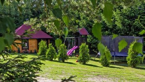 Una cabaña de madera con techo rojo, rodeada por un patio cubierto de césped con un columpio y un trampolín.