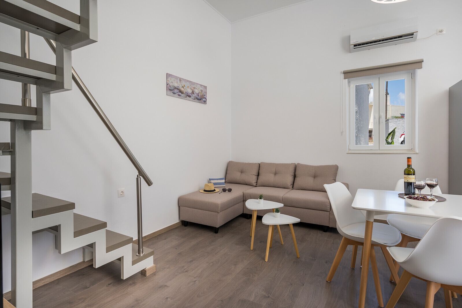 Un salon moderne avec un escalier, un canapé, une table à manger et une fenêtre donnant sur un beau paysage.
