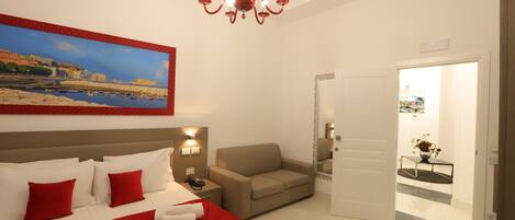 Una habitación de hotel con una cama, un sofá, un cuadro, una araña y una puerta que da a un pasillo.