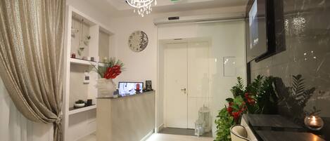 A modern reception area with a chandelier, a clock, a TV, and a reception desk with a computer monitor.
