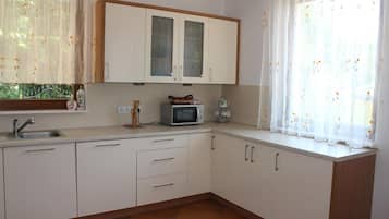 Een keuken met witte kastjes, een magnetron, een spoelbak en een raam met bloemen gordijnen.