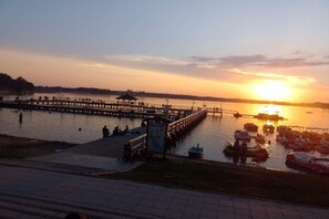 Une jetée au bord de l’eau, avec des gens et des bateaux, un panneau indicateur et un coucher de soleil.