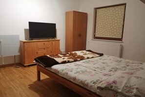 Une chambre à coucher avec un lit, une armoire, un téléviseur posé sur une commode et un radiateur.
