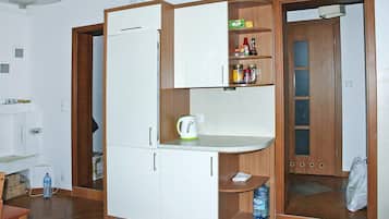 A compact kitchen with a built-in refrigerator, a kettle, and a shelf with condiments.