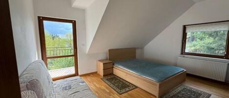 Ein Schlafzimmer mit schrägen Wänden, einem Bett, einem Nachttisch, einem Fenster und Blick ins Grüne.