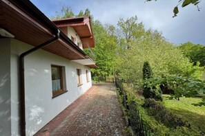 Un bâtiment doté d’un toit en pente, d’un chemin en briques menant à l’entrée et d’un espace jardin verdoyant avec des arbres.