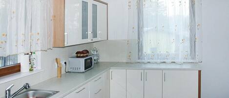 A kitchen with white cabinets, a microwave, a sink, and a window with floral curtains.