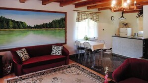 A cozy room with a red sofa, a dining table with chairs, a kitchen area, and a large painting of a lake. - Cottage by Lake Dabrowa with Fishing (Kalbornia)