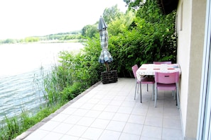 En terrasse med et bord og stole, en lille parasol og udsigt til vand.