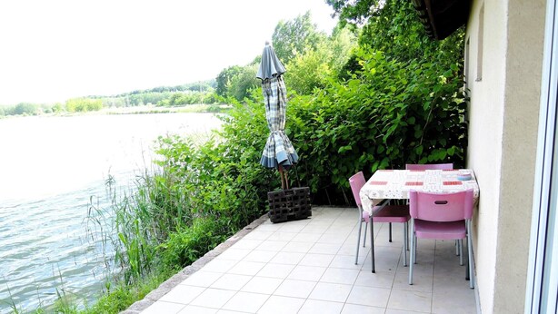 Un patio con mesa y sillas, una sombrilla pequeña y vista hacia un cuerpo de agua.
