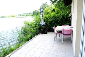 Un patio con mesa y sillas, una sombrilla pequeña y vista hacia un cuerpo de agua.