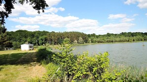 Vista a un lago con una cabaña pequeña y un bosque denso al fondo.