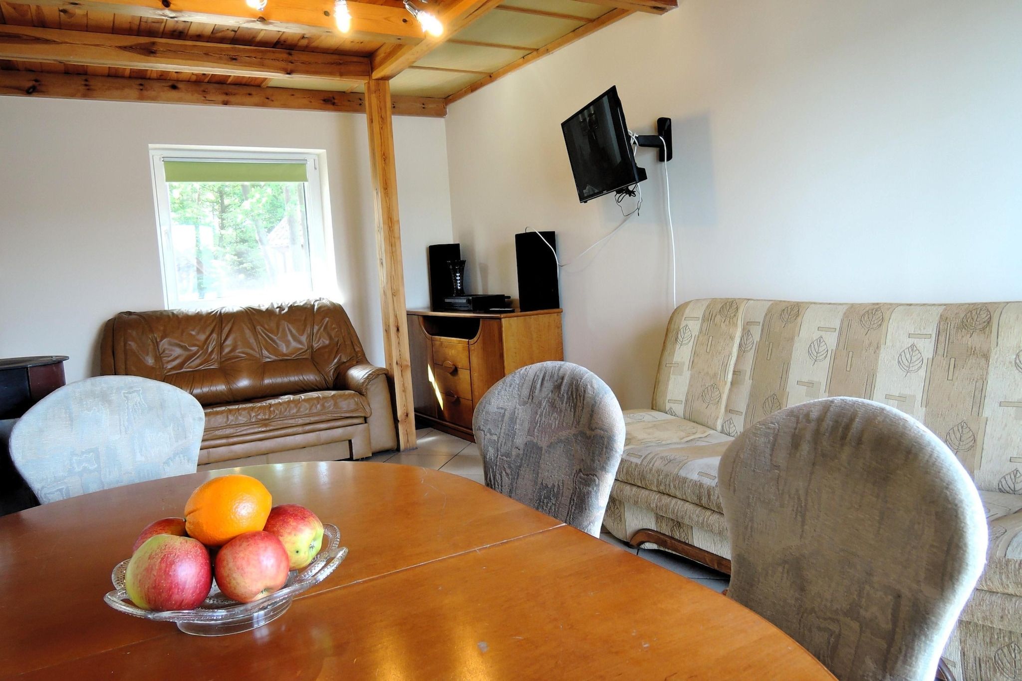Une pièce comprenant une table à manger en bois, un canapé en cuir marron, un canapé à motifs et un téléviseur fixé au mur.