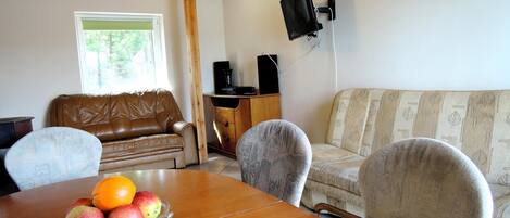 Una habitación con una mesa de comedor de madera, un sofá de cuero marrón, un sofá estampado y un televisor montado en la pared.
