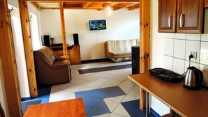 Una cocina acogedora con techo de madera, un televisor montado en la pared, un sofá y una mesa de comedor con una tetera.