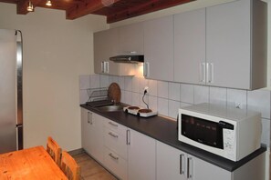 Une cuisine compacte avec des meubles blancs, un four à micro-ondes, une bouilloire et une table en bois.