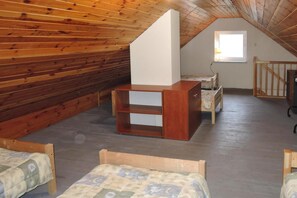 Een kamer met houten wanden, een schuine kap, een klein raam en twee houten bedden.