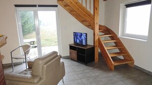 Ein Wohnzimmer mit einer Holztreppe, einem Fernseher, einer Couch und einem Fenster.
