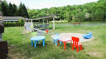 Un espace extérieur aménagé avec des tables et des chaises, un pavillon couvert et un étang en arrière-plan.