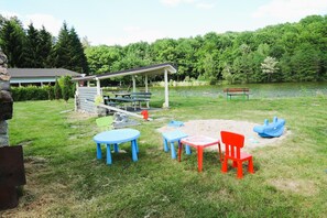 Un área de estar al aire libre con mesas y sillas, un pabellón cubierto y un estanque al fondo.