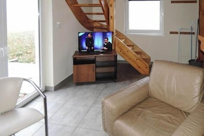 A living room with a television on a wooden stand, a beige leather sofa, and a staircase.