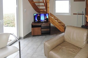 Un salon avec un canapé, un téléviseur posé sur un meuble en bois, un escalier et une vue à travers une porte vitrée.