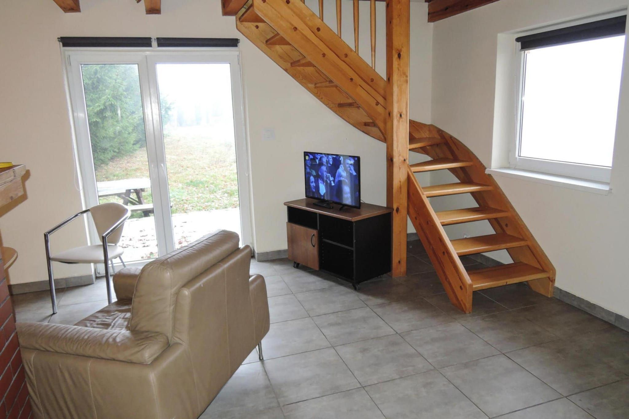 A living room with a wooden staircase, a television on a stand, a sofa, and a chair.