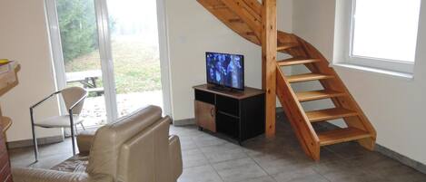 A living room with a wooden staircase, a television on a stand, a sofa, and a chair.