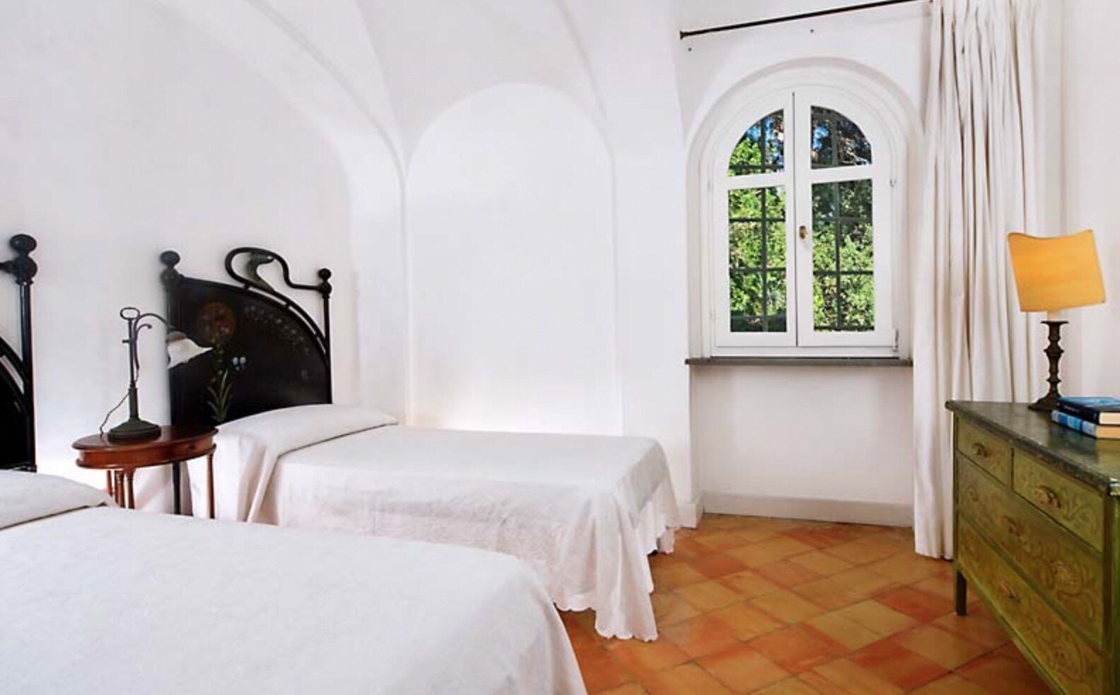 Una habitación con dos camas, una ventana con cortinas, una lámpara y un aparador.
