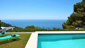 A swimming pool with a view of the sea, a grassy area with lounge chairs, and a clear sky. - Villa Paradiso, Capri (capri)