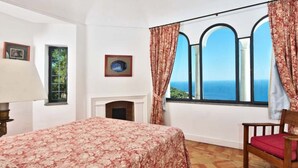 A bedroom with a bed, a fireplace, a window with curtains, and a chair. - Villa Paradiso, Capri (capri)