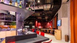 A modern bar area with a bar counter, seating, and a variety of bottles on shelves. - Ibis Tbilisi Stadium (Tbilisi)