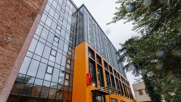 A modern building with a glass facade and orange accents, featuring a prominent entrance and outdoor seating area. - Ibis Tbilisi Stadium (Tbilisi)