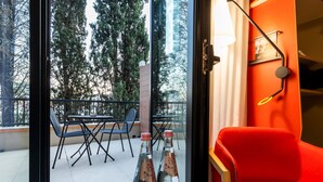 A room with a red chair, a table with bottles, and a balcony with chairs and a table. - Ibis Tbilisi Stadium (Tbilisi)