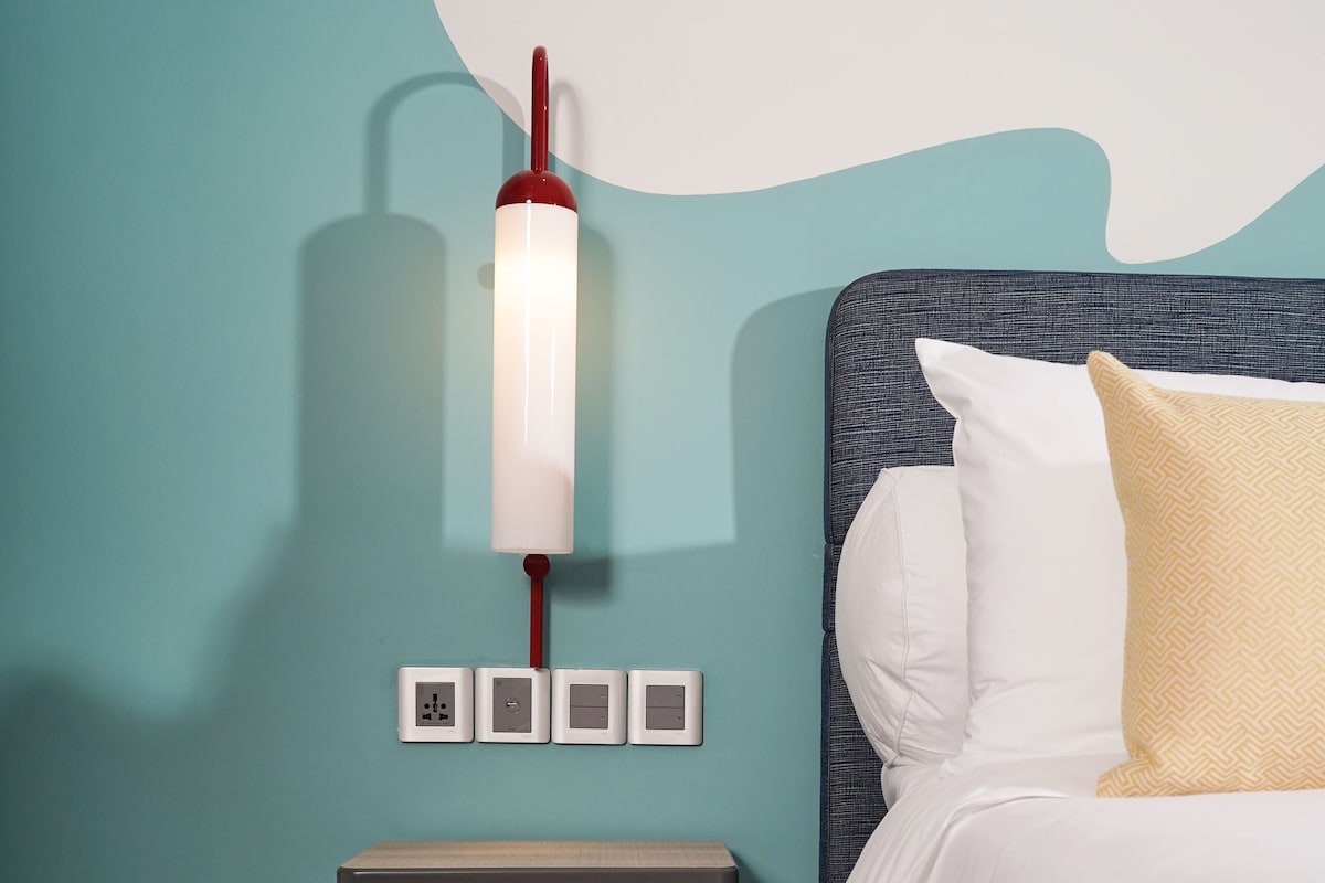 Un dormitorio ordenado con cama, mesita de noche y lámpara de pared.