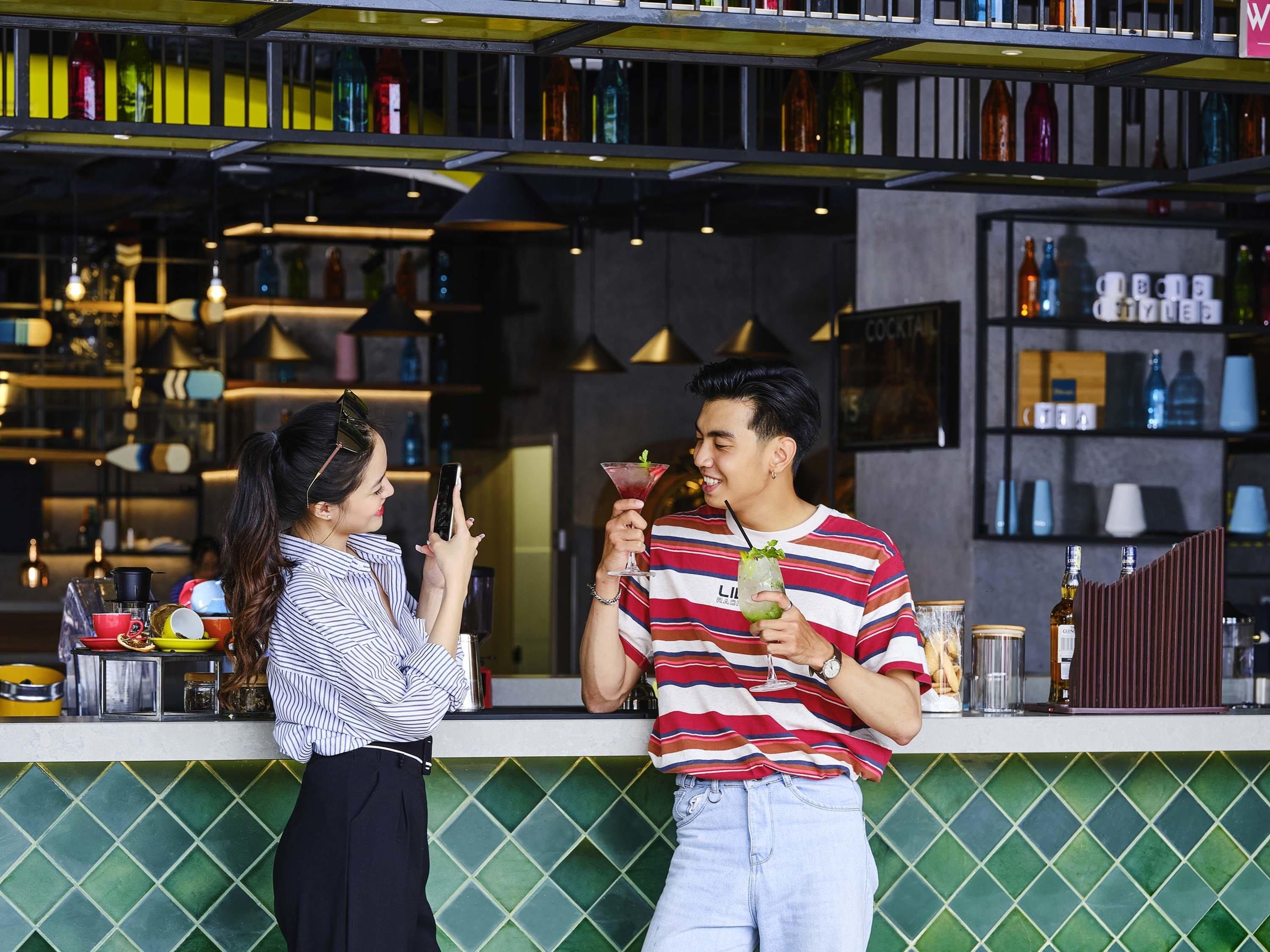 Zona de bar con estanterías llenas de botellas y vasos, una barra con un menú y un salpicadero de azulejos verdes.