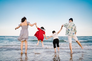 Una familia de cuatro salta de la mano en aguas poco profundas en la playa.