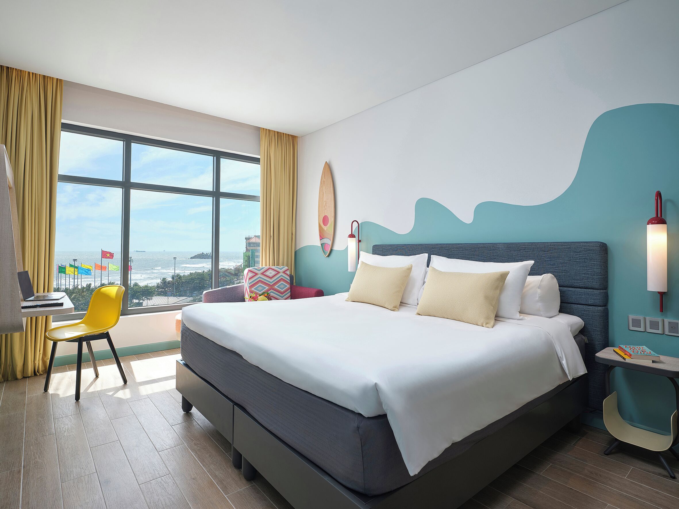 Habitación de hotel con una cama grande, un escritorio con una computadora portátil, una silla y vistas al océano.
