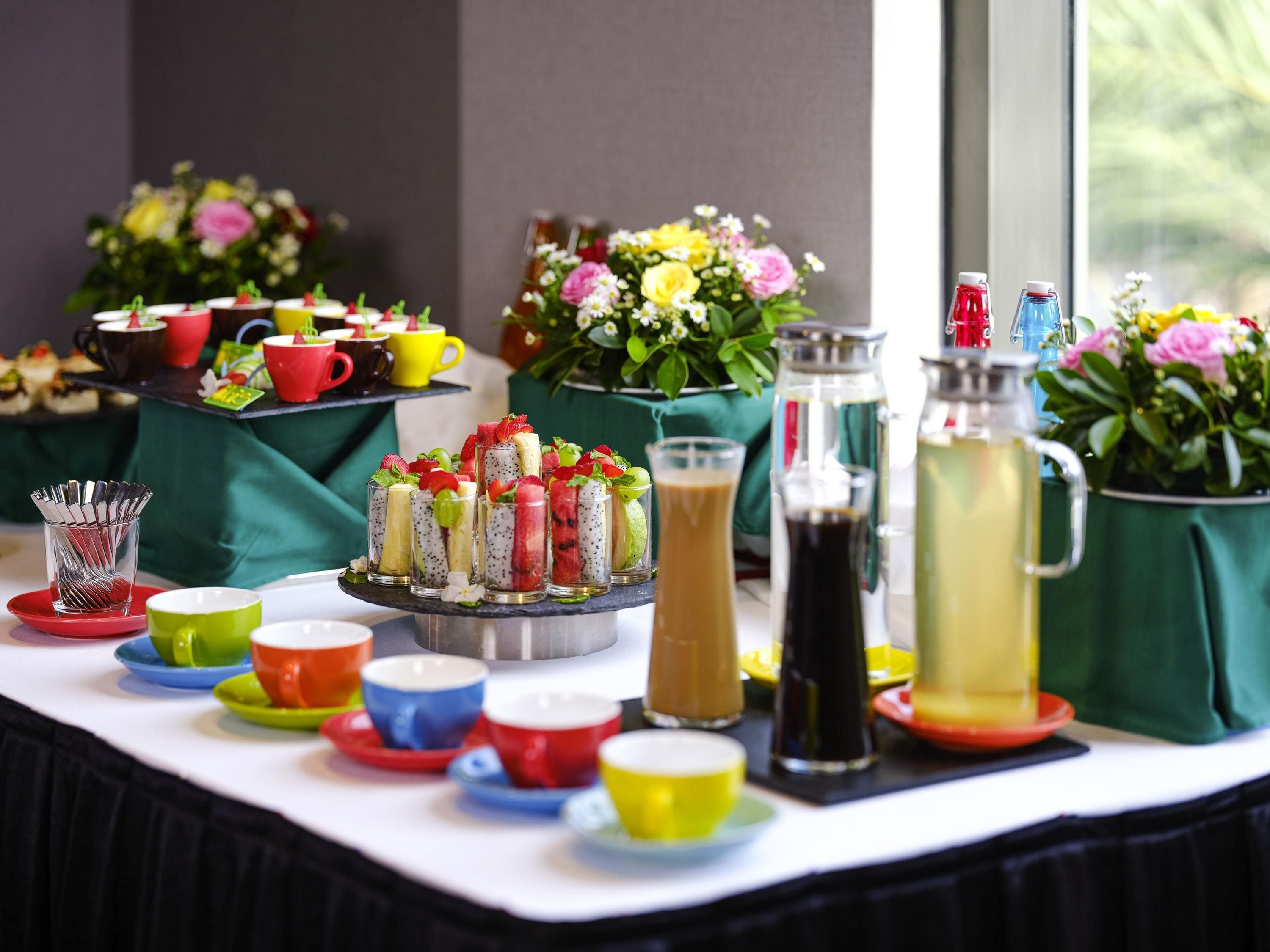 A buffet table with various food items, colorful cups, and a pitcher of iced tea.