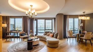 A modern living room with a round coffee table, a sofa, a dining area with chairs, and a large window offering a city view. - Sofitel Istanbul Taksim (Istanbul)