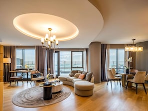 A modern living room with a round coffee table, a sofa, a dining area with chairs, and a large window offering a city view. - Sofitel Istanbul Taksim (Istanbul)