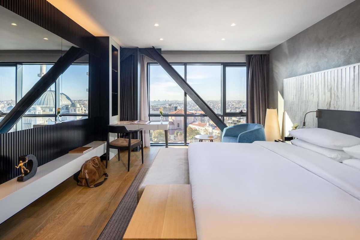 Una habitación de hotel moderna con una cama grande, un escritorio y vistas a un paisaje urbano.