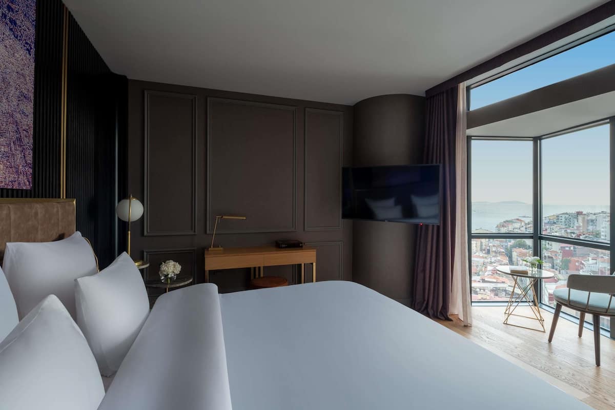 Una habitación de hotel moderna con una cama grande, un escritorio, un televisor de pantalla plana y vistas a la ciudad.