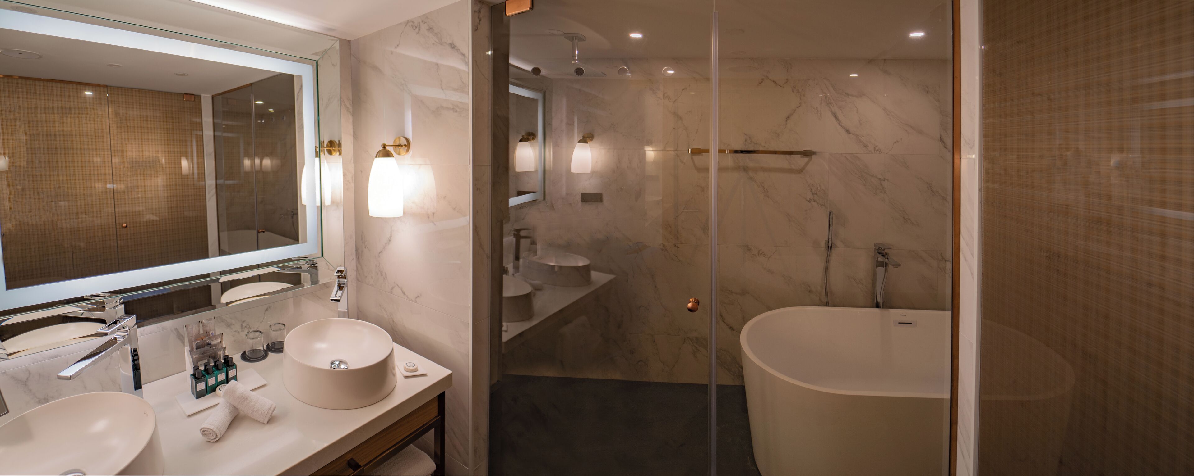 A modern bathroom with a large mirror, two sinks, a bathtub, and a glass-enclosed shower area.