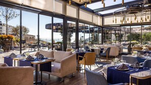 A modern restaurant with large windows, outdoor seating, and a view of the city. - Sofitel Istanbul Taksim (Istanbul)