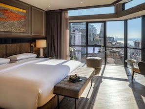 A hotel room with a large bed, a bench, a small table, and a view of the city. - Sofitel Istanbul Taksim (Istanbul)