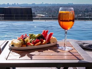 A table with a fruit platter and a glass of amber-colored beverage, overlooking a body of water with a cityscape in the background. - Sofitel Istanbul Taksim (Istanbul)
